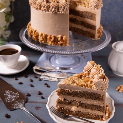 Coffee and walnut cake a strati con crema al caffè, ciuffi decorativi e noci tritate, con una fetta tagliata in primo piano