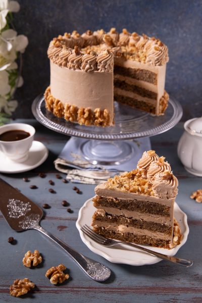 Coffee and walnut cake a strati con crema al caffè, ciuffi decorativi e noci tritate, con una fetta tagliata in primo piano
