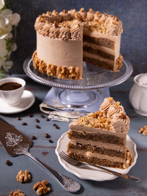 Coffee and walnut cake a strati con crema al caffè, ciuffi decorativi e noci tritate, con una fetta tagliata in primo piano