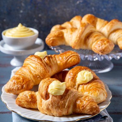 Cornetti sfogliati alla crema dorati e fragranti, guarniti con ciuffi di crema pasticcera