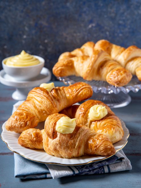 Cornetti sfogliati alla crema dorati e fragranti, guarniti con ciuffi di crema pasticcera