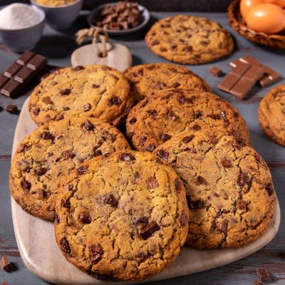 Crumbl cookies con gocce di cioccolato fondente, dorati e fragranti, serviti su tagliere