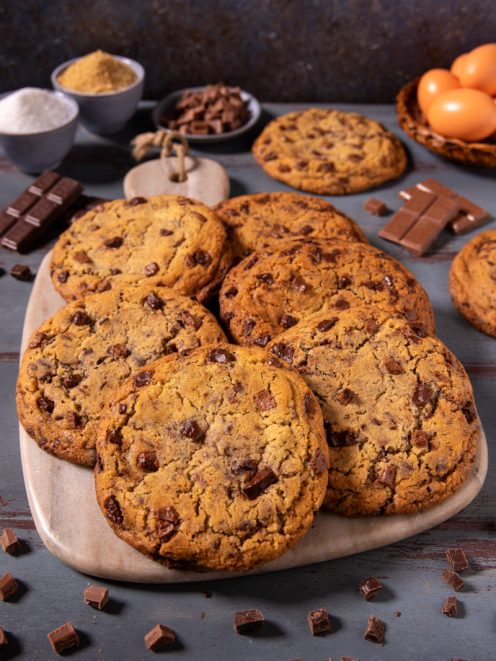 Crumbl cookies con gocce di cioccolato fondente, dorati e fragranti, serviti su tagliere