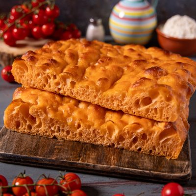 Focaccia con acqua di pomodoro, due pezzi sovrapposti con superficie dorata alveolata e mollica soffice, tra pomodorini freschi
