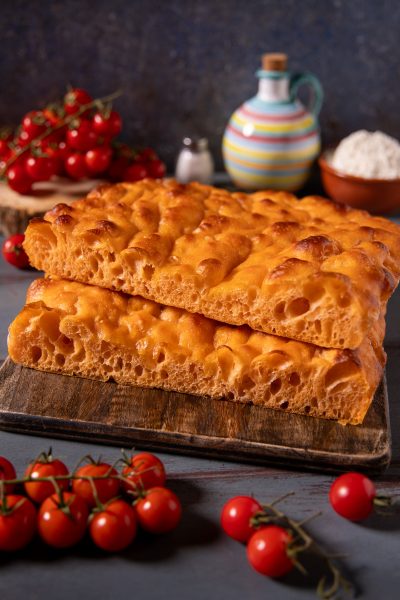 Focaccia con acqua di pomodoro, due pezzi sovrapposti con superficie dorata alveolata e mollica soffice, tra pomodorini freschi