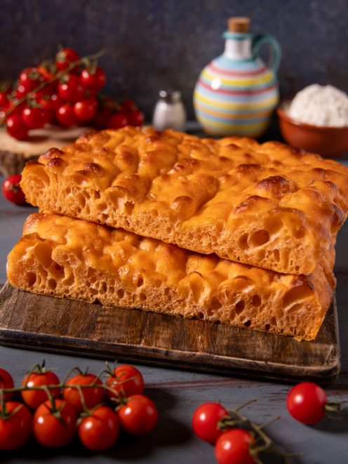 Focaccia con acqua di pomodoro, due pezzi sovrapposti con superficie dorata alveolata e mollica soffice, tra pomodorini freschi