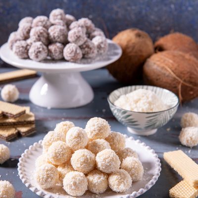 Palline di cocco bianche e al cioccolato ricoperte di cocco grattugiato accanto a wafer e cocchi freschi