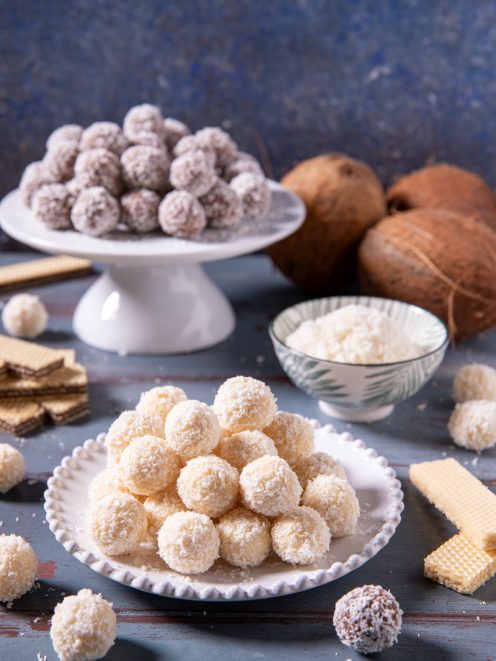 Palline di cocco bianche e al cioccolato ricoperte di cocco grattugiato accanto a wafer e cocchi freschi