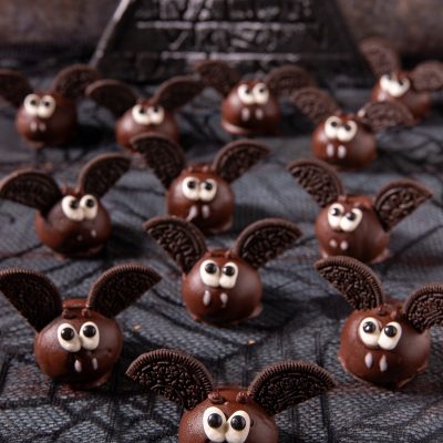 Pipistrelli di Halloween: palline ricoperte di cioccolato con ali di biscotto al cacao, occhietti e zanne di zucchero