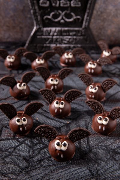 Pipistrelli di Halloween: palline ricoperte di cioccolato con ali di biscotto al cacao, occhietti e zanne di zucchero
