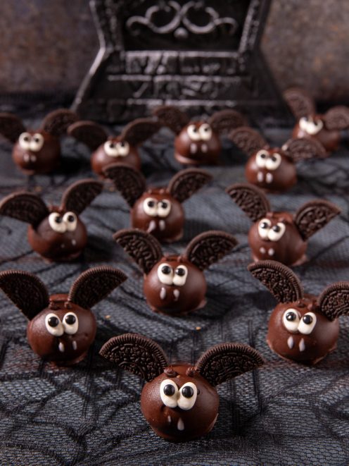 Pipistrelli di Halloween: palline ricoperte di cioccolato con ali di biscotto al cacao, occhietti e zanne di zucchero
