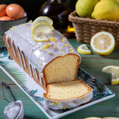 Plumcake al limone con glassa colante, fette di limone e scorza grattugiata, tagliato a fette