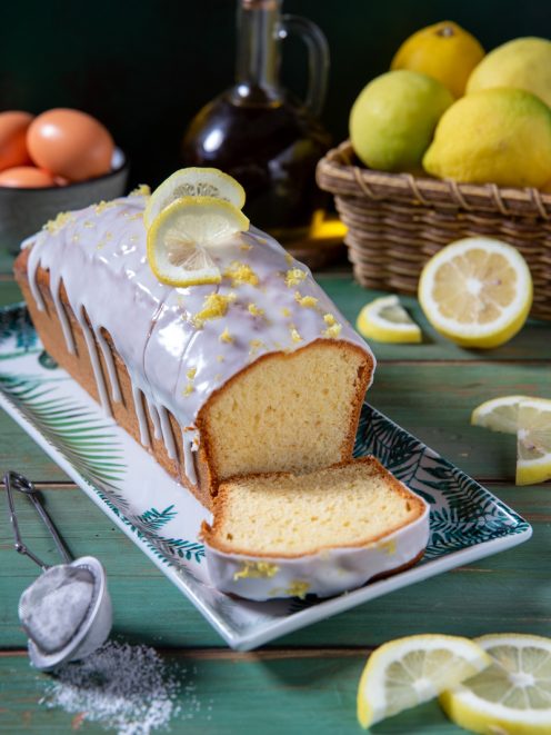 Plumcake al limone con glassa colante, fette di limone e scorza grattugiata, tagliato a fette