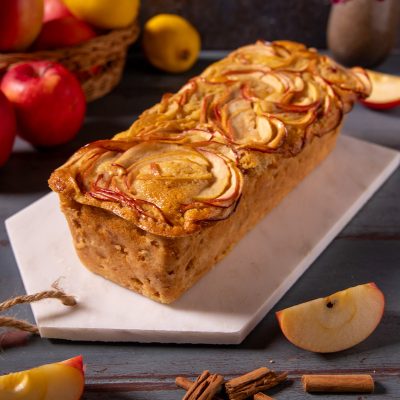 Plumcake alle mele con fettine disposte a rosetta sulla superficie dorata e bastoncini di cannella