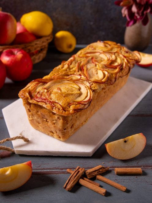 Plumcake alle mele con fettine disposte a rosetta sulla superficie dorata e bastoncini di cannella