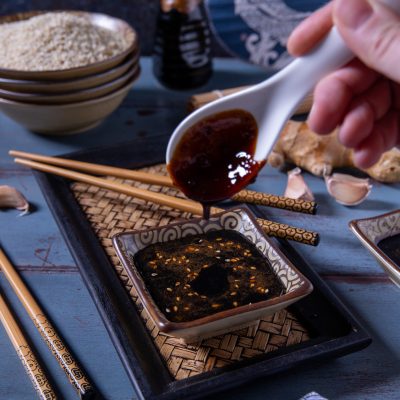 Salsa teriyaki versata da un cucchiaio in una ciotolina cosparsa di sesamo tostato