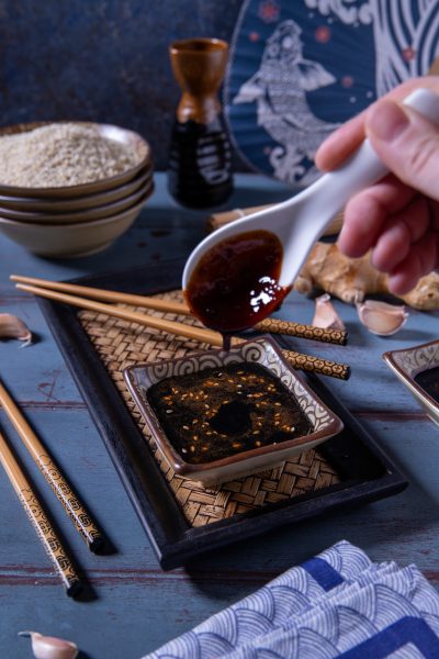 Salsa teriyaki versata da un cucchiaio in una ciotolina cosparsa di sesamo tostato