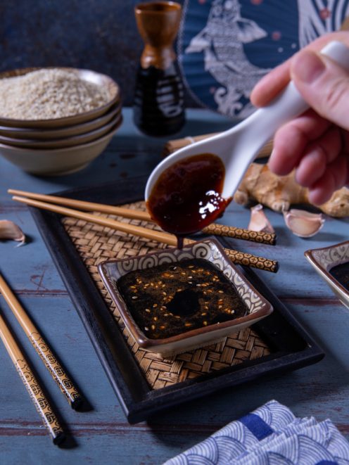 Salsa teriyaki versata da un cucchiaio in una ciotolina cosparsa di sesamo tostato