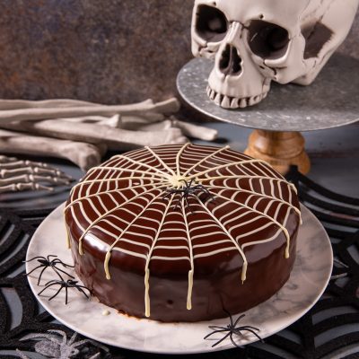 Torta ragnatela con glassa al cioccolato lucida decorata da fili di cioccolato bianco a forma di ragnatela e un ragno nero al centro