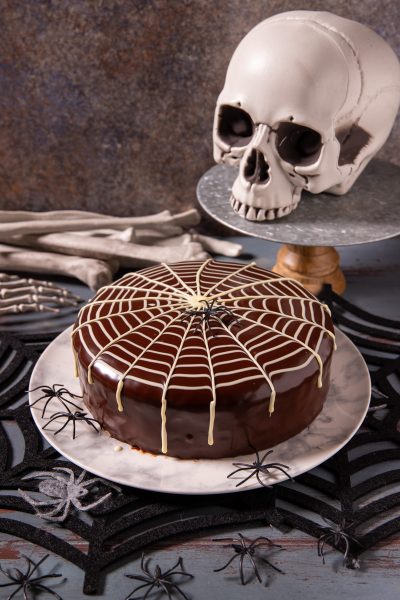 Torta ragnatela con glassa al cioccolato lucida decorata da fili di cioccolato bianco a forma di ragnatela e un ragno nero al centro