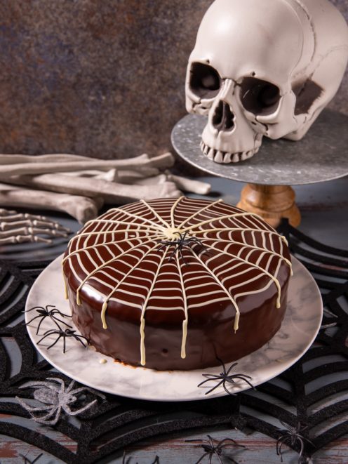 Torta ragnatela con glassa al cioccolato lucida decorata da fili di cioccolato bianco a forma di ragnatela e un ragno nero al centro