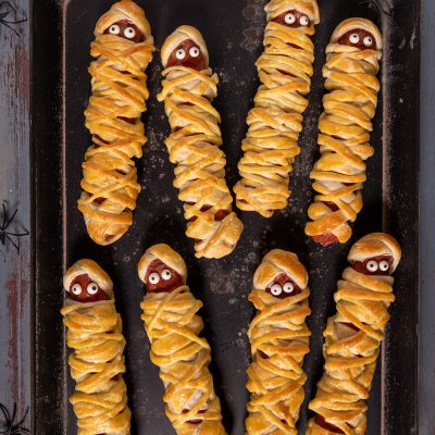 Wurstel mummia in pasta sfoglia con occhietti di zucchero disposti su una teglia per Halloween