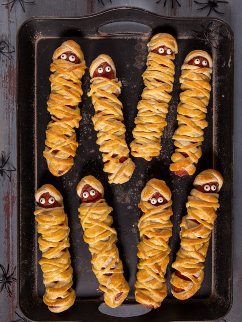 Wurstel mummia in pasta sfoglia con occhietti di zucchero disposti su una teglia per Halloween