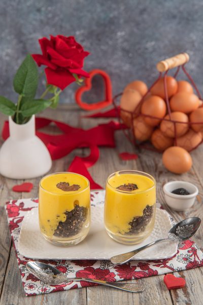 Bicchierini di zabaione con crumble al tartufo, strati di crema gialla su briciole scure e scaglia di tartufo in superficie