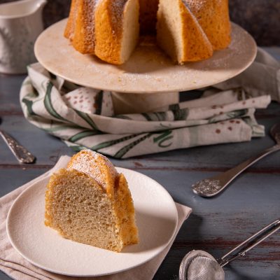 Ciambella senza uova spolverata di zucchero a velo, con una fetta dalla mollica soffice in primo piano