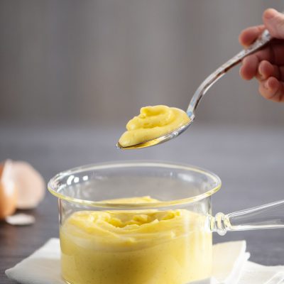 Crema pasticcera alla vaniglia con puntini di bacca, sollevata con un cucchiaio da un pentolino di vetro