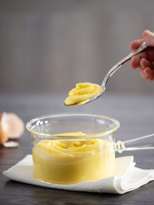Crema pasticcera alla vaniglia con puntini di bacca, sollevata con un cucchiaio da un pentolino di vetro