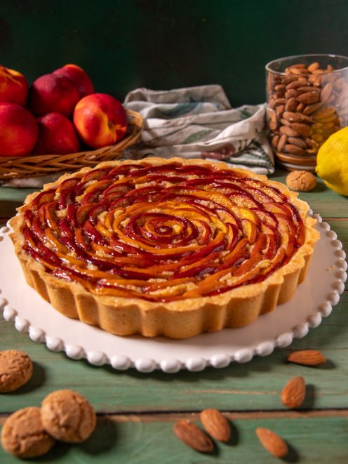 Crostata di pesche e amaretti con fettine di pesca disposte a spirale su base di frolla e crema, servita intera