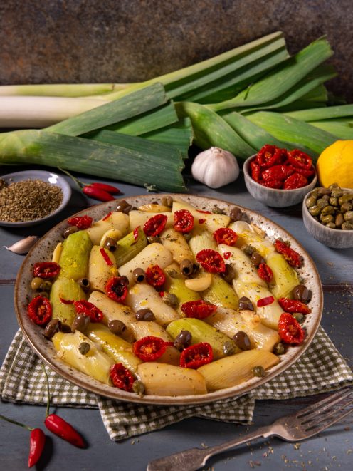 Porri alla mediterranea a pezzi con pomodori secchi, olive, capperi e spicchi d'aglio, serviti in un piatto da portata