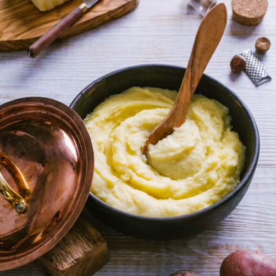 Purè Bimby cremoso e setoso lavorato a vortice, con cucchiaio di legno, accanto a burro, noce moscata e patate rosse