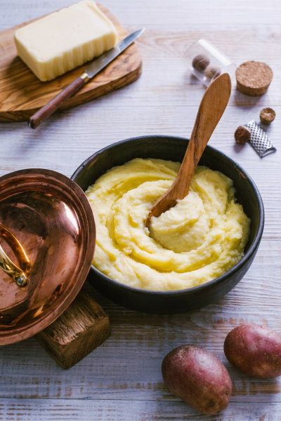 Purè Bimby cremoso e setoso lavorato a vortice, con cucchiaio di legno, accanto a burro, noce moscata e patate rosse