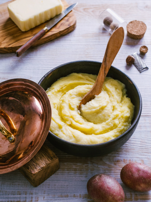 Purè Bimby cremoso e setoso lavorato a vortice, con cucchiaio di legno, accanto a burro, noce moscata e patate rosse