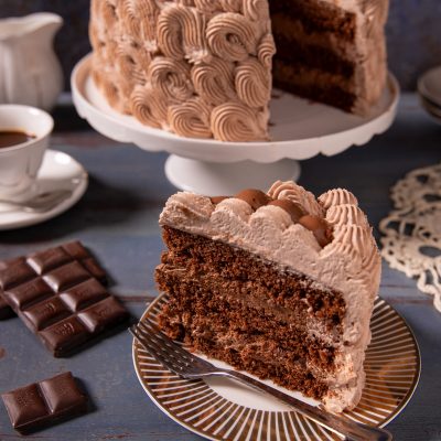 Torta chantilly al cioccolato a strati con crema montata a ciuffi e una fetta servita in primo piano