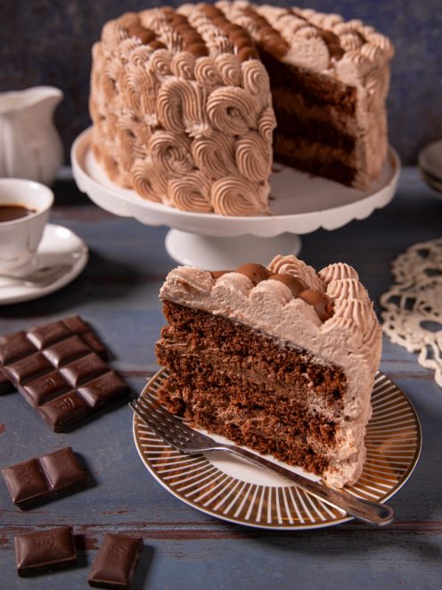 Torta chantilly al cioccolato a strati con crema montata a ciuffi e una fetta servita in primo piano