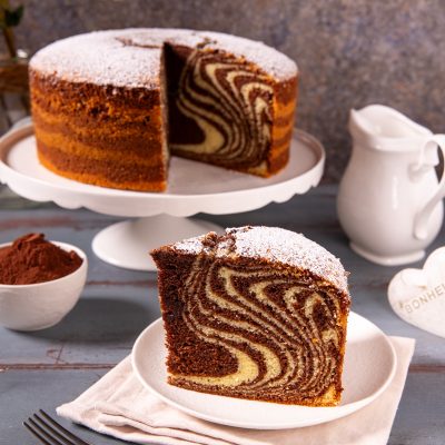 Torta zebrata con spolverata di zucchero a velo, fetta in primo piano che mostra le caratteristiche strisce di cacao e impasto chiaro