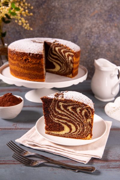 Torta zebrata con spolverata di zucchero a velo, fetta in primo piano che mostra le caratteristiche strisce di cacao e impasto chiaro