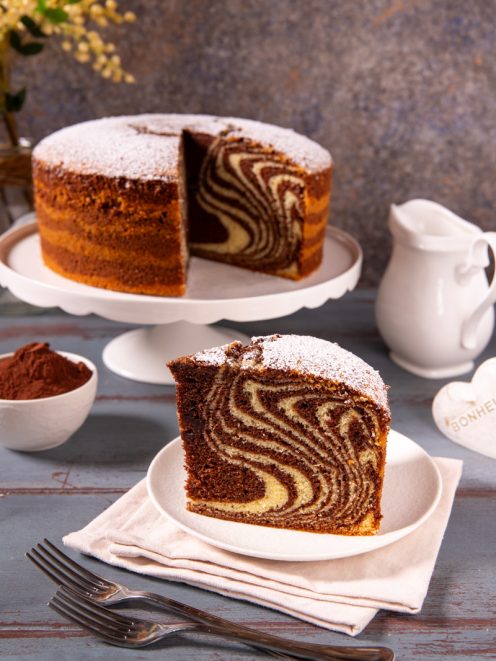 Torta zebrata con spolverata di zucchero a velo, fetta in primo piano che mostra le caratteristiche strisce di cacao e impasto chiaro