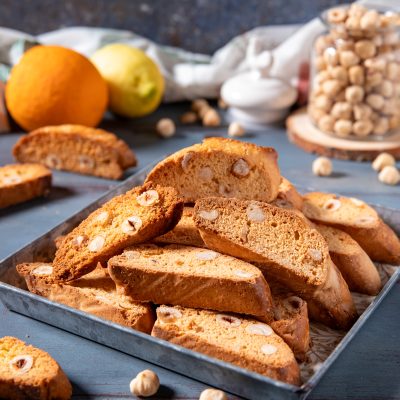 Tozzetti croccanti con nocciole intere, tagliati a fette e impilati in un vassoio, con nocciole sparse intorno